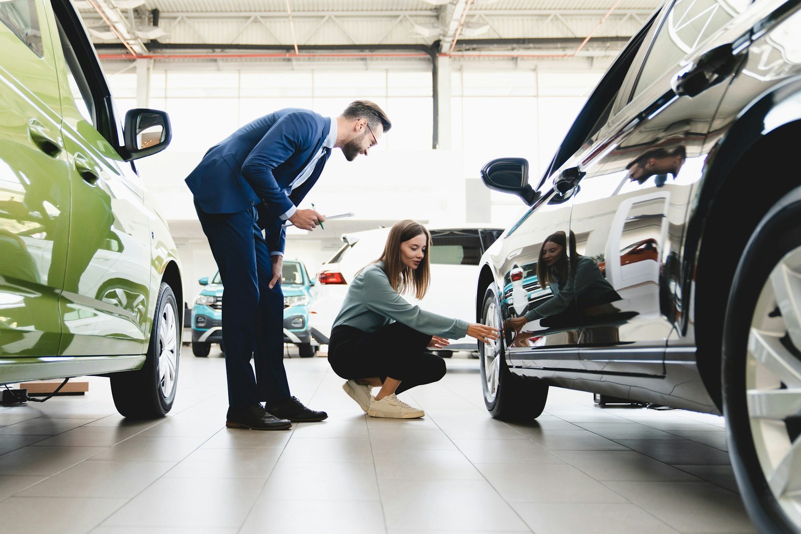 Customer choosing new car, checking its options, tire, wheels while shop assistant helping choose it